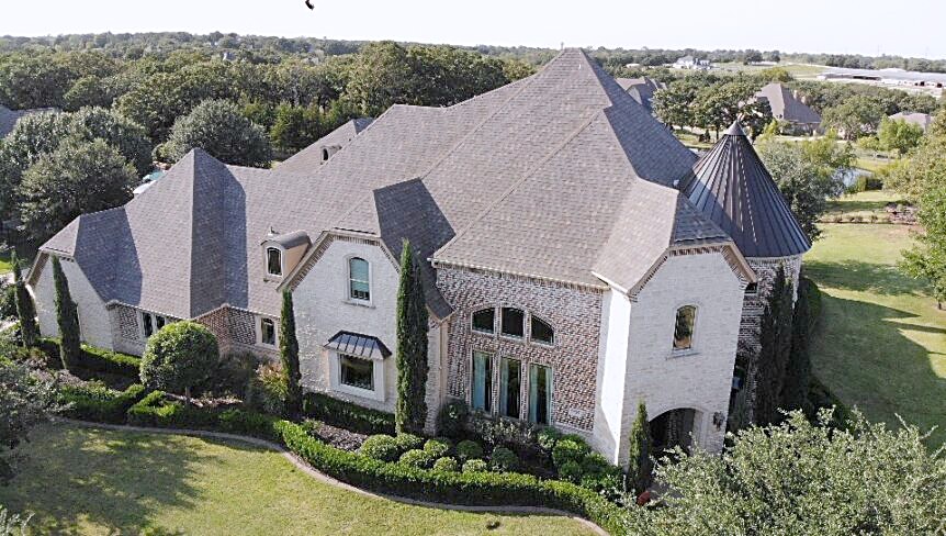 Aerial view of a finished multi-plane shingle roof on a stone and brick home